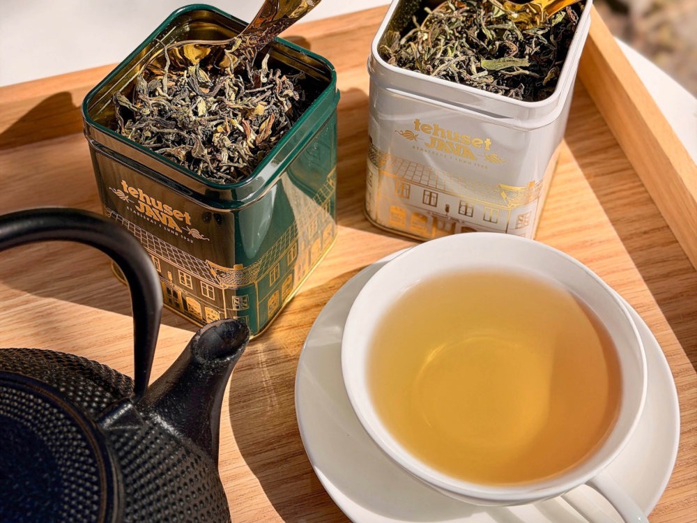 Darjeeling-te i kopp med två fulla teburkar på träbricka
