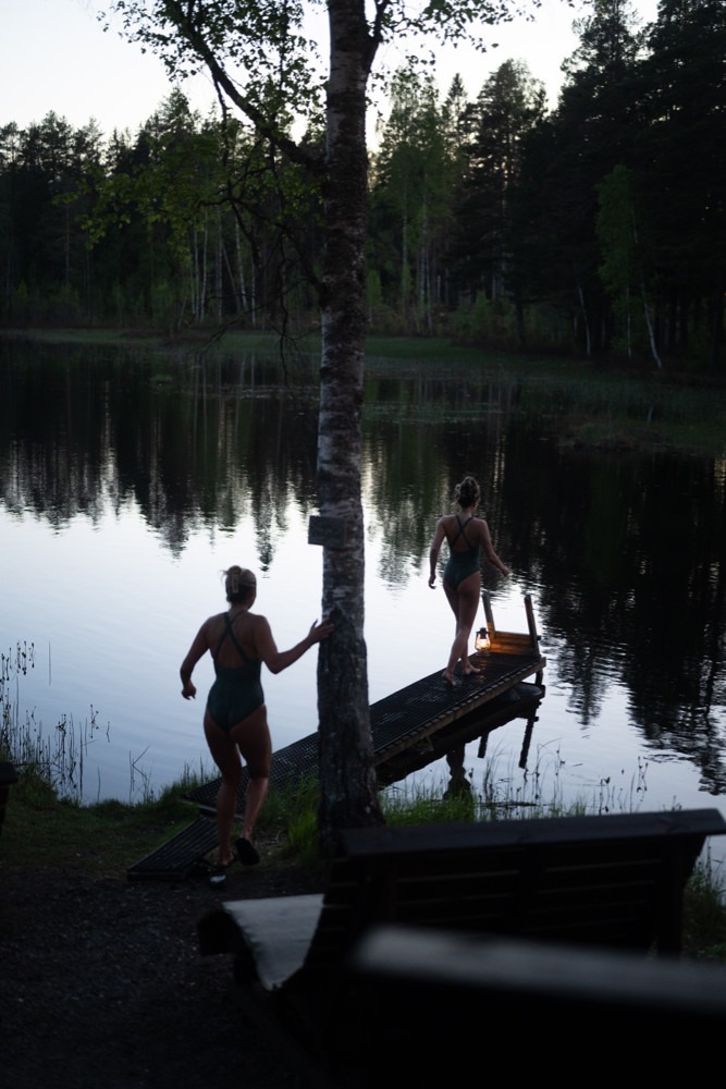 två kvinnor i badkläder går på brygga med lykta, skymning