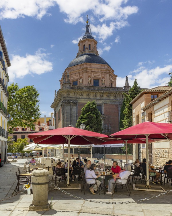 Utomhuscafé med röda parasoller framför en kyrka i Madrid.