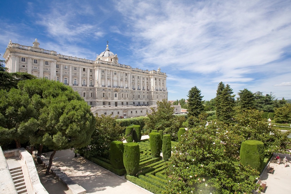 Kungliga palatset i Madrid med anlagda trädgårdar under en blå himmel.