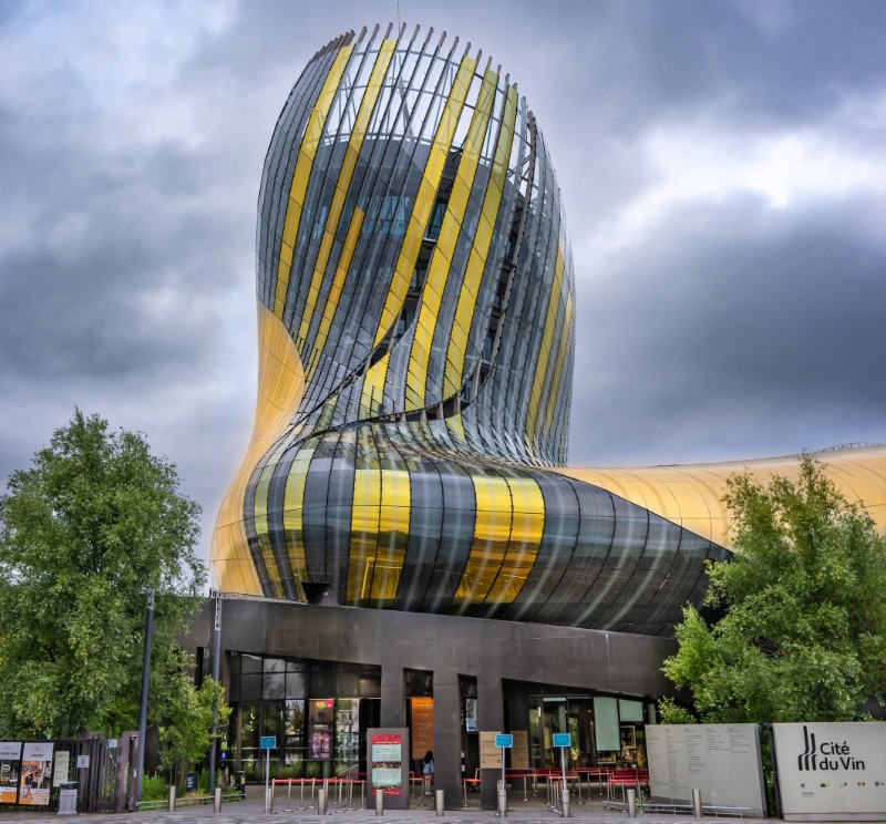 La Cité du Vin i Bordeaux, en modern byggnad med en böljande form i guld och glas mot en molnig himmel.