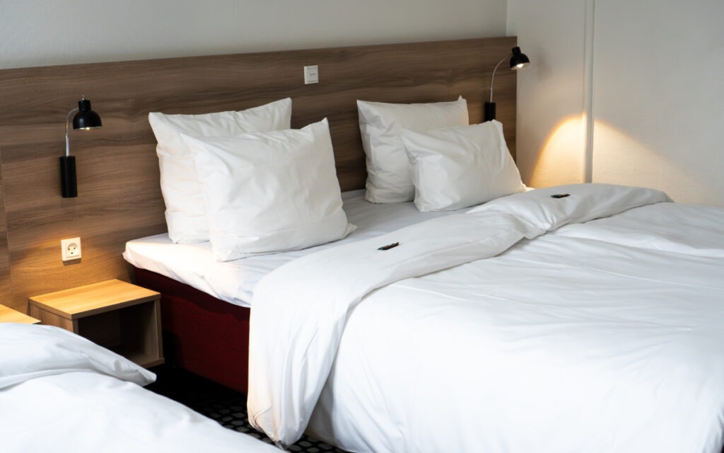 Ett hotellrum med två enkelsängar med vita lakan och kuddar, trägavel och svarta vägglampor.