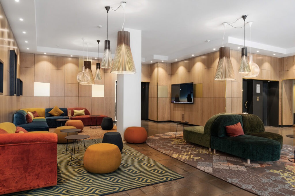 En modern hotelllobby med färgglada sammetsmöbler, träpanelväggar och hängande lampor i bambu.