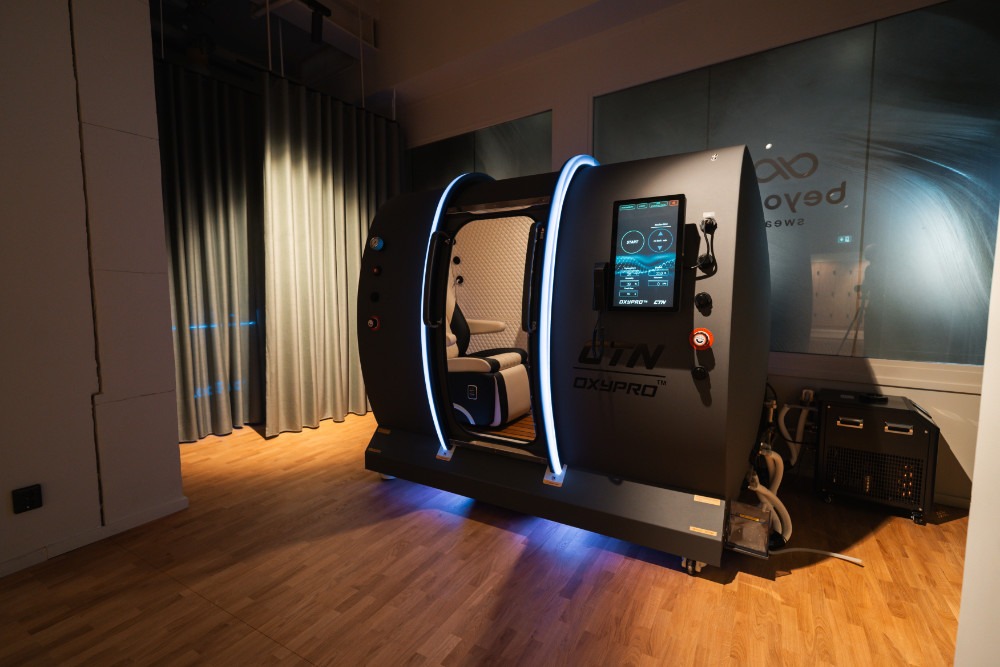 Hyperbar syrekammare med blå LED-list och pekskärm, bredvid en kompressor.